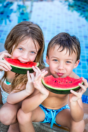 Summer vacation - children eat watermelon by the pool