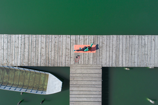 Drone view on a woman exercising on the lake pier