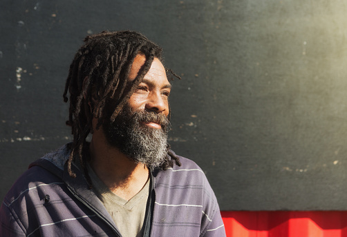 A dreadlocked homeless person smiles, daydreaming of better times.