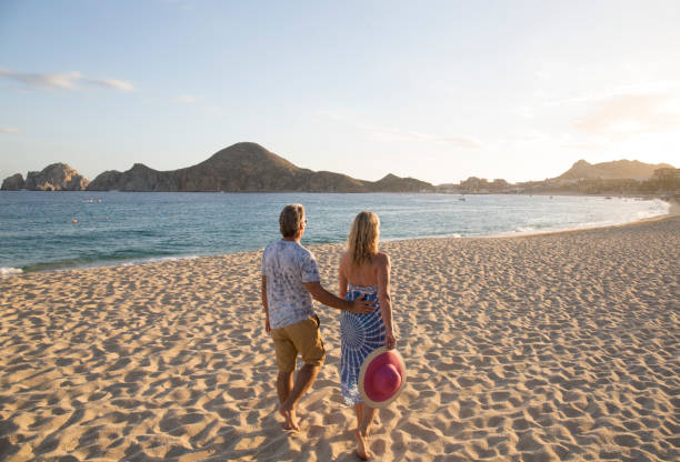Couple walking towards hills on beach by the sea at sunset They are walking away from the camera and no one else is on the beach,  Los Cabos area, Baja California Sur cabo san lucas stock pictures, royalty-free photos & images
