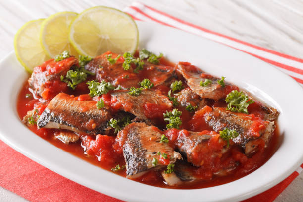Braised sardines in tomato sauce with lime and parsley close-up. horizontal Braised sardines in tomato sauce with lime and parsley close-up on a plate. horizontal sardine photos stock pictures, royalty-free photos & images