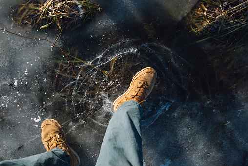 man stay on the cracked ice and kick it lag on the clear lake with straw under ice