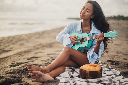 Woman sitting at the beach and playing ukulele