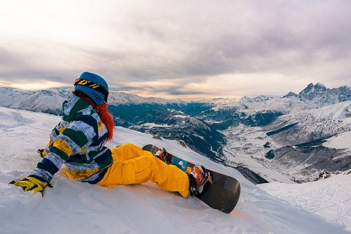 snowboarder is sitting on the mountain and watching down with snowboard and watching the view