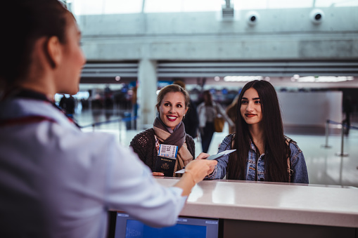 Mother and daughter travelling together doing check-in for flight at airline desk in airport