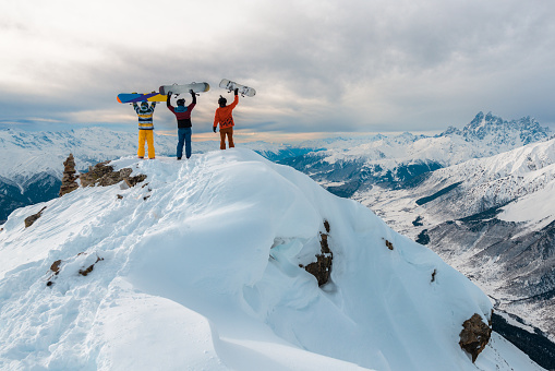 There are three men standing on the top of mountain with snowboards