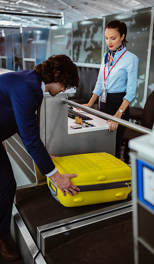 Young man putting suitcase on weight scale conveyor belt at airline check-in counter