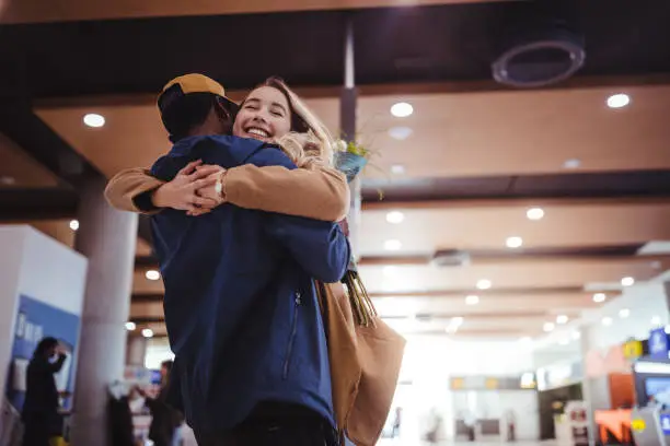 Happy multi-ethnic couple meeting and embracing at airport after flight arrival
