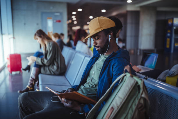 wieloetniczni pasażerowie siedzący na ławce i czekający na lotnisku - airport tourist airport lounge young men zdjęcia i obrazy z banku zdjęć