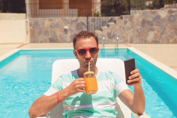 Modern man using cellphone while drinking juice on the pool. stock photo