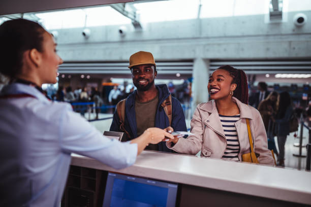 Young passengers doing check-in for flight at airport Young African-American couple doing check-in at airline check-in counter at international airport airport check in counter photos stock pictures, royalty-free photos & images
