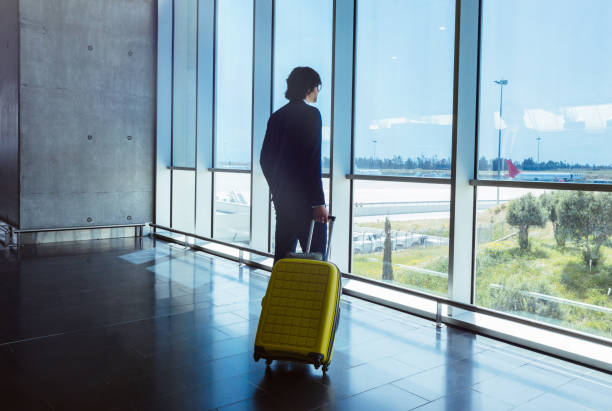 istock Young businessman with suitcase looking through window at airport 959525724
