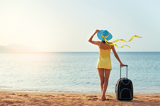 Beautiful young woman with a hat standing with suitcase on the wonderful sea background, concept of time to travel, with space for your text.