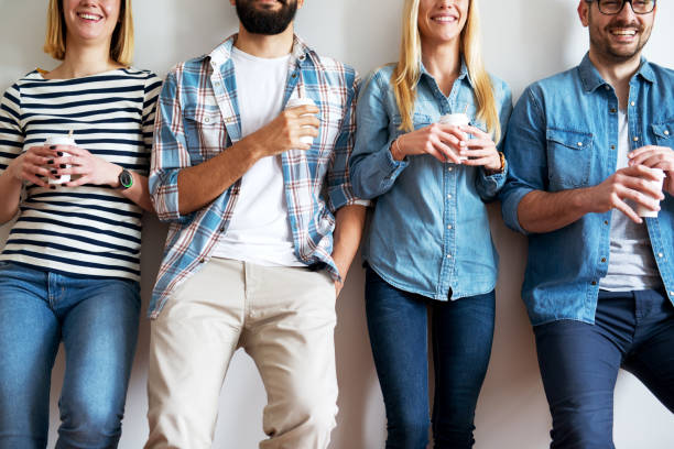 istock Close up view of young joyful people leaned against the wall having a break and drinking coffee from a paper cups. 959532336