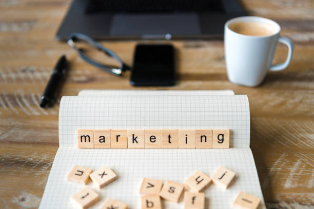 istock Closeup on notebook over wood table background, focus on wooden blocks with letters making Marketing word 959532850