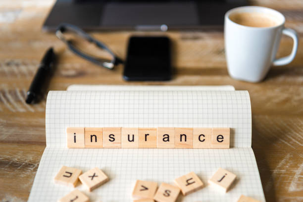 istock Closeup on notebook over wood table background, focus on wooden blocks with letters making Insurance word 959535938