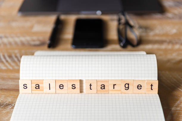 istock Closeup on notebook over wood table background, focus on wooden blocks with letters making Sales Target words 959536604