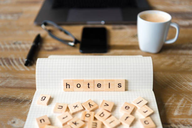 istock Closeup on notebook over wood table background, focus on wooden blocks with letters making Hotels word 959538142