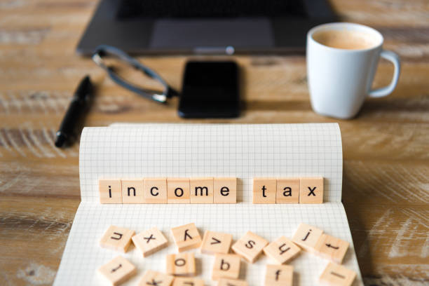 istock Closeup on notebook over wood table background, focus on wooden blocks with letters making Income Tax words 959538480