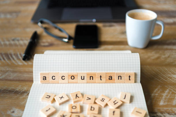 istock Closeup on notebook over wood table background, focus on wooden blocks with letters making Accountant word 959542780