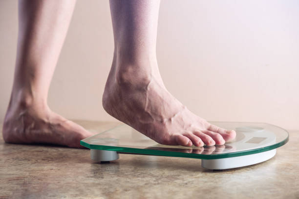 istock Female feet standing on electronic scales for weight control on light background. Concept of sports training, diets 959543210