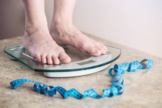 istock Female feet standing on electronic scales for weight control on light background. Concept of sports training, diets 959543224