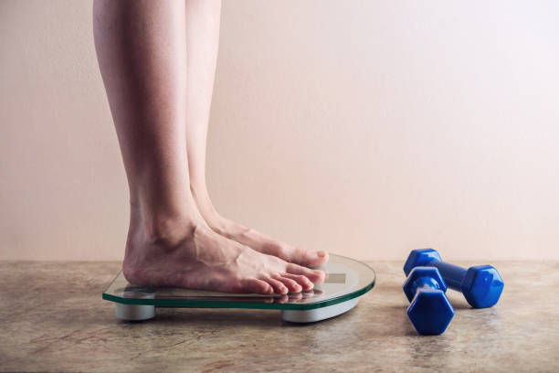 istock Female feet standing on electronic scales for weight control on light background. Concept of sports training, diets 959543246
