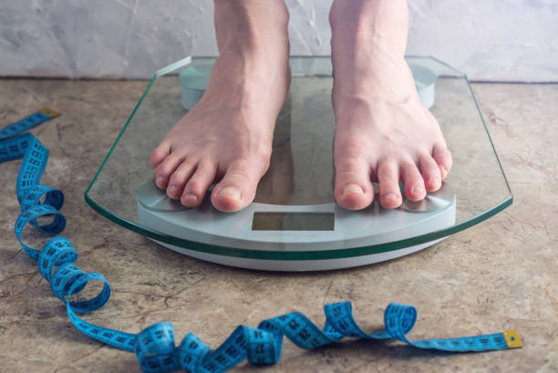 istock Female feet standing on electronic scales for weight control on light background. Concept of sports training, diets 959543256