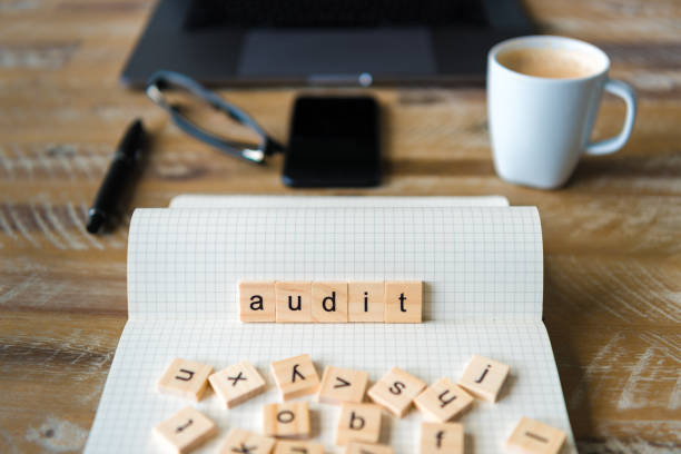 istock Closeup on notebook over wood table background, focus on wooden blocks with letters making Audit word 959543282