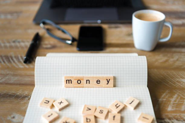 istock Closeup on notebook over wood table background, focus on wooden blocks with letters making Money word 959546958