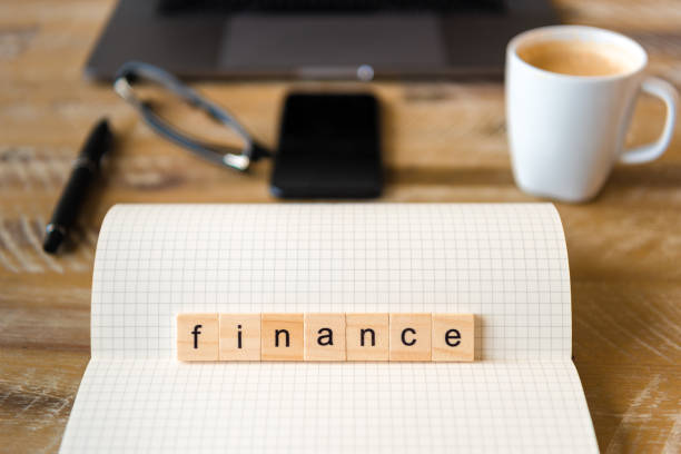 istock Closeup on notebook over wood table background, focus on wooden blocks with letters making Finance word 959550840