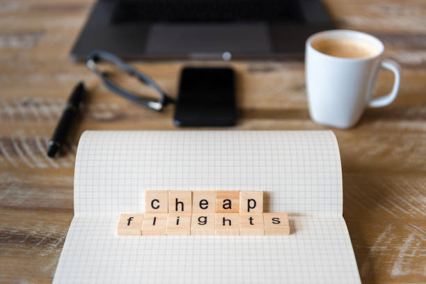 istock Closeup on notebook over wood table background, focus on wooden blocks with letters making Cheap Flights words 959552068