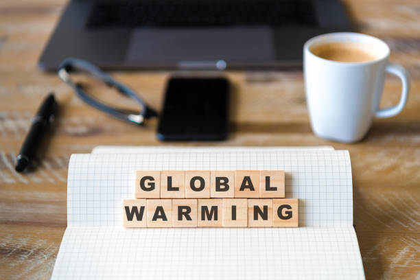 istock Closeup on notebook over wood table background, focus on wooden blocks with letters making GLOBAL WARMING words 959552456