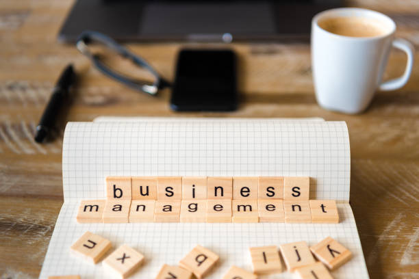 istock Closeup on notebook over wood table background, focus on wooden blocks with letters making Business Management words 959555190