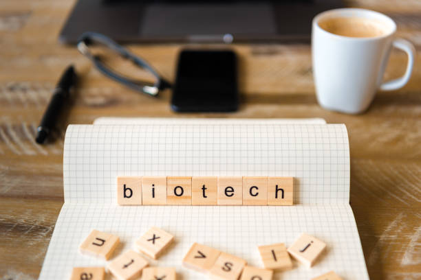 istock Closeup on notebook over wood table background, focus on wooden blocks with letters making Biotech word 959555456