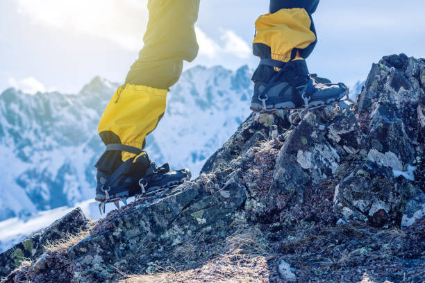 Climber in crampons stands on the rocks in front of the entrance to the peak on the background of the snowy mountains. stock photo