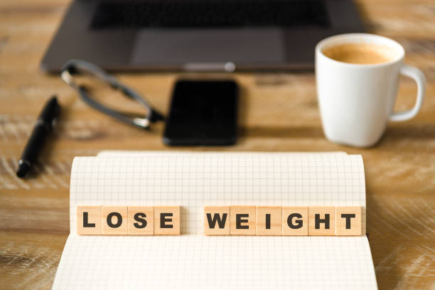 istock Closeup on notebook over wood table background, focus on wooden blocks with letters making LOSE WEIGHT words 959555888