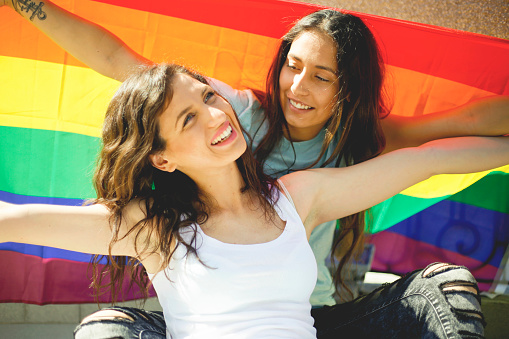 LGBT Lesbian couple moments happiness concept. Holding rainbow flag outdoors
