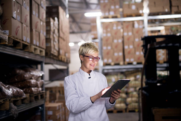 istock Young cheerful female worker is using her tablet in factory storage area. 959560092