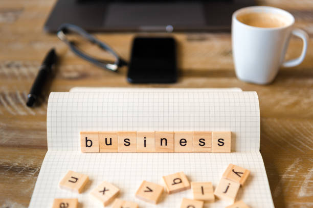 istock Closeup on notebook over wood table background, focus on wooden blocks with letters making Business word 959565192