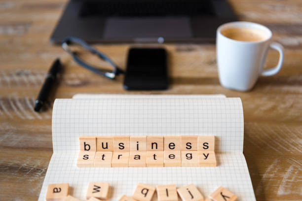 istock Closeup on notebook over wood table background, focus on wooden blocks with letters making Business Strategy words 959566920