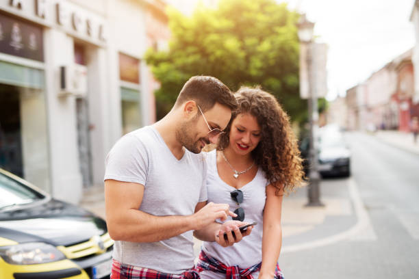 istock Young cheerful loving couple is using a phone while standing on a street. 959573192
