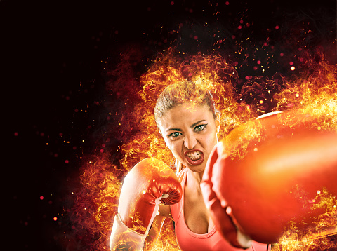 Aggressive female athlete boxing with gloves surrounded by fire and flames