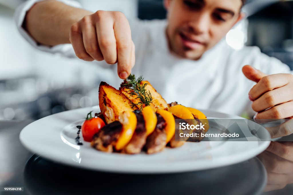Making dinner into a masterpiece Shot of a young chef decorating meal in the kitchen Chef Stock Photo