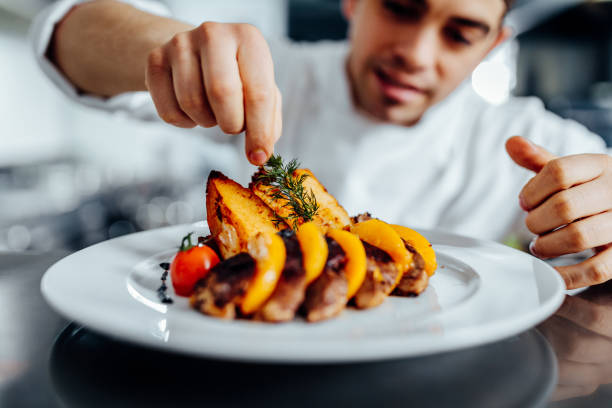 Making dinner into a masterpiece Shot of a young chef decorating meal in the kitchen service occupation photos stock pictures, royalty-free photos & images