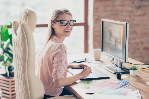 istock Charming, pretty woman holding tablet pen, having colorful palette, using digitizer, sitting on armchair at desk in work station, making, drawing sketch, looking at camera 959590980