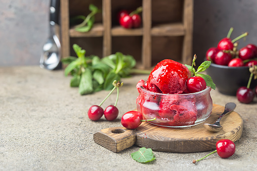 Delicious cherry ice cream in a glass bowl with fresh cherries on wooden cutting board