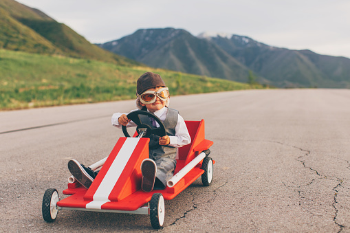 A young business boy dressed in business attire and race goggles sits in a push cart on a rural road in Utah. This business boy loves racing and competing and working for the success of his business. He smiles at the camera before the race starts.