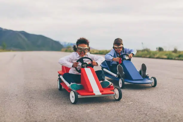 A young business girl races a boy dressed in business attire and race goggles in a push cart down a rural road in Utah. These business children love racing and competing and working hard for the success of their business. The young business boy struggles to beat the girl.