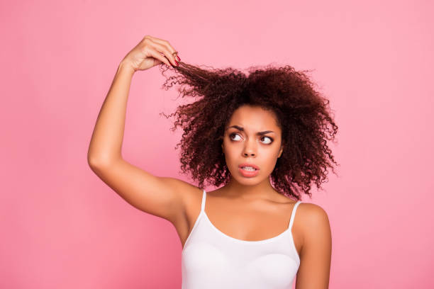 portrait of pretty, worry, attractive girl examine, look her curly hair, holding strand with hand, she want straight perfect, soft, shine hair, need treatment and therapy  isolated on pink background - female emotional stress african ethnicity loss imagens e fotografias de stock